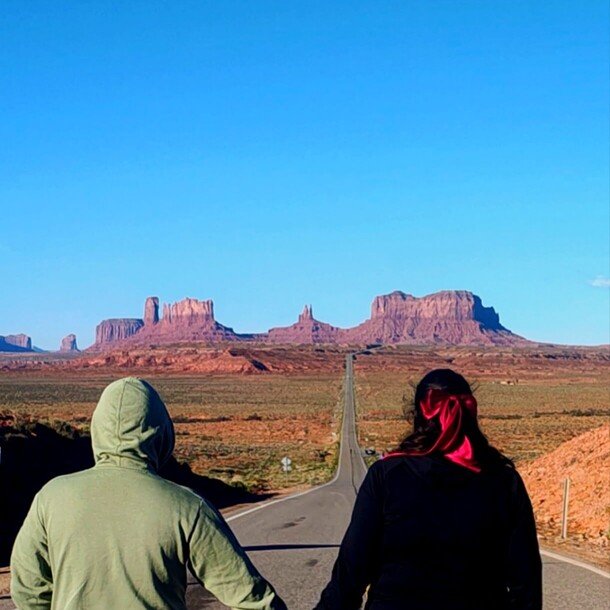 Joana y su pareja de espaldas contemplando la famosa carretera recta que lleva hacia las formaciones rocosas de Monument Valley.