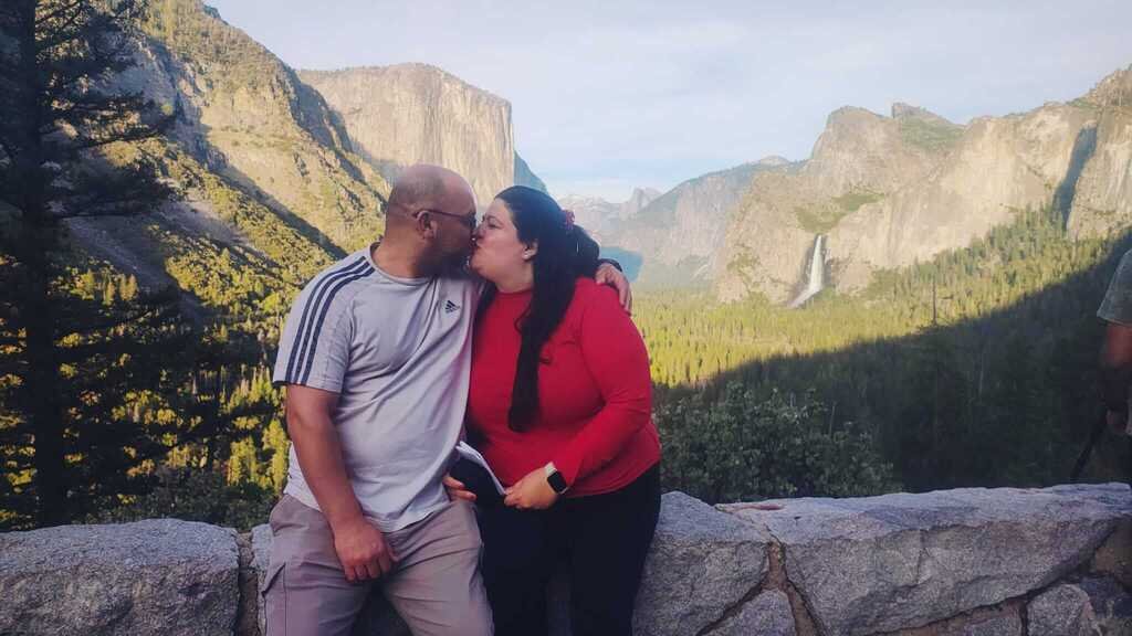 Joana y su pareja besándose con el impresionante paisaje del Parque Nacional de Yosemite y sus cascadas al fondo.