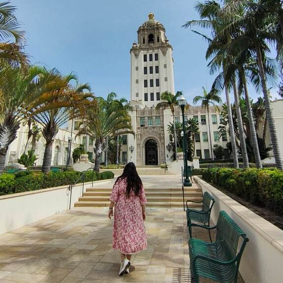 Mujer con vestido rosa caminando hacia el Ayuntamiento de Beverly Hills rodeada de palmeras.